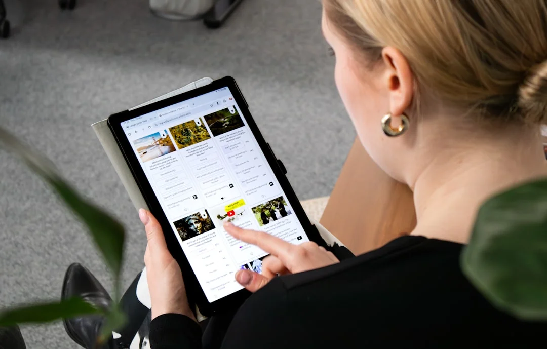 Hands using a tablet beside a laptop in a home office setting, showcasing online browsing.